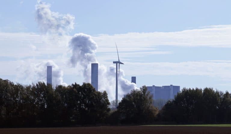 A power plant running on a fossil fuel with a wind turbine in the foreground