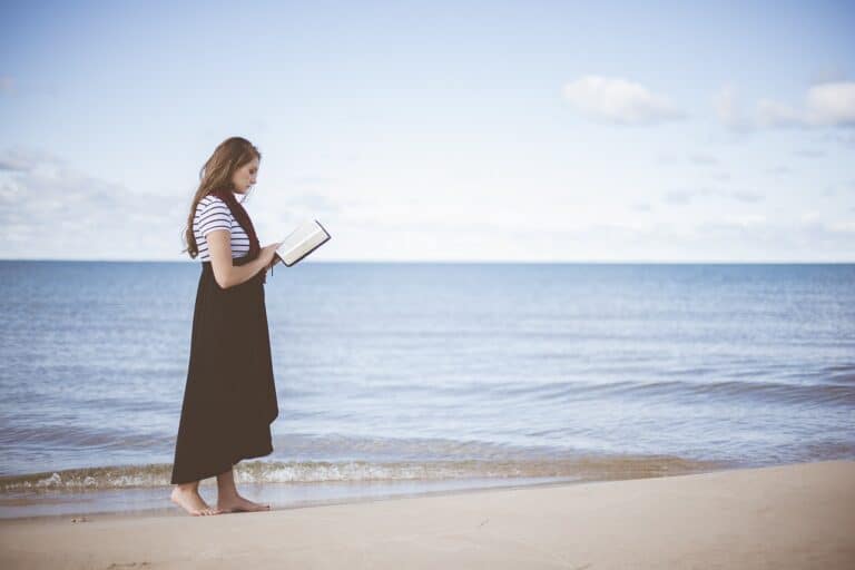 A young woman near the ocean reading one of her favorite beach reads